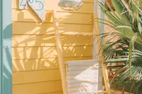 Casita exterior detail with a yellow wall, outdoor lantern, and chair surrounded by tropical plants at Boardwalk Boutique Hotel Aruba.