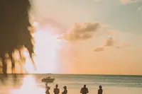 Silhouettes of people standing on the beach at sunset with the sun reflecting on the ocean near Boardwalk Boutique Hotel Aruba.