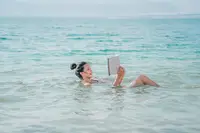 Woman floating in calm ocean water while reading a book near Boardwalk Boutique Hotel Aruba.