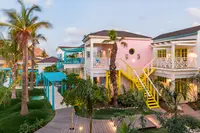 View of colorful two-story casita buildings and staircases surrounded by palm trees and tropical landscaping at Boardwalk Boutique Hotel Aruba.