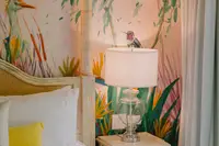 Cozy bedroom with a white bed, bedside table and lamp, and tropical wallpaper at Boardwalk Boutique Hotel Aruba.