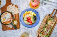 Overhead breakfast spread at Boardwalk Boutique Hotel Aruba with fresh fruit bowl, toast, and open-faced sandwich on a marble table.