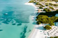 Drone view of a tropical coastline with turquoise water, white sand beach, and beach umbrellas lining the shore.