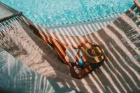 A hammock above the pool with a drink tray, casting striped shadows across the scene at Boardwalk Boutique Hotel Aruba.
