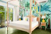Coco Deluxe Casita bedroom at Boardwalk Boutique Hotel Aruba with four-poster bed and tropical mural wall.