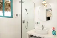 Palapa Lodge bathroom at Boardwalk Boutique Hotel Aruba with walk-in shower, vanity sink, and round mirror.