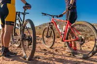 Two cyclists with mountain bikes on a desert trail in Aruba under a clear blue sky.