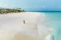 Person walking along Eagle Beach in Aruba in the morning, with white sand and turquoise water.