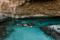 Swimmer in the turquoise Bushiri Natural Pool in Aruba, surrounded by rocky cliffs.