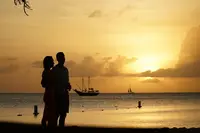 Couple silhouette watching the sunset on Palm Beach, Aruba, with calm sea and sailboats in the distance.