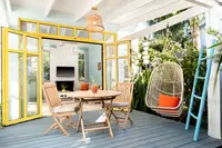 Private casita patio with a dining table, folding chairs, and a hanging egg chair outside a bright yellow-framed room at Boardwalk Boutique Hotel Aruba.