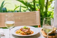 Outdoor table set with plated dishes and glasses of white wine, surrounded by tropical greenery at Boardwalk Boutique Hotel Aruba.