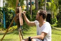 Artist Armando Goedgedrag painting on an easel during a live session in the tropical garden at Boardwalk Boutique Hotel Aruba.