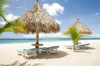 Palapa umbrellas and lounge chairs on a white sand beach with turquoise water and a blue sky at Boardwalk Boutique Hotel Aruba.