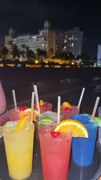 Colorful cocktails at Bugaloe Beach Bar in Aruba at night, served with the oceanfront lights in the background.