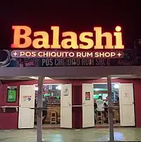 Exterior of the Balashi Pos Chiquito Rum Shop in Aruba, pictured at night with the storefront sign.