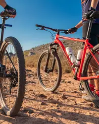 Two cyclists with mountain bikes on a desert trail in Aruba under a clear blue sky.