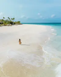 Person walking along Eagle Beach in Aruba in the morning, with white sand and turquoise water.
