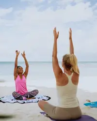 Two women doing beach yoga on Palm Beach, Aruba near Boardwalk Boutique Hotel slow summer campaign 