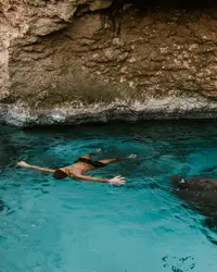 Swimmer in the turquoise Bushiri Natural Pool in Aruba, surrounded by rocky cliffs.